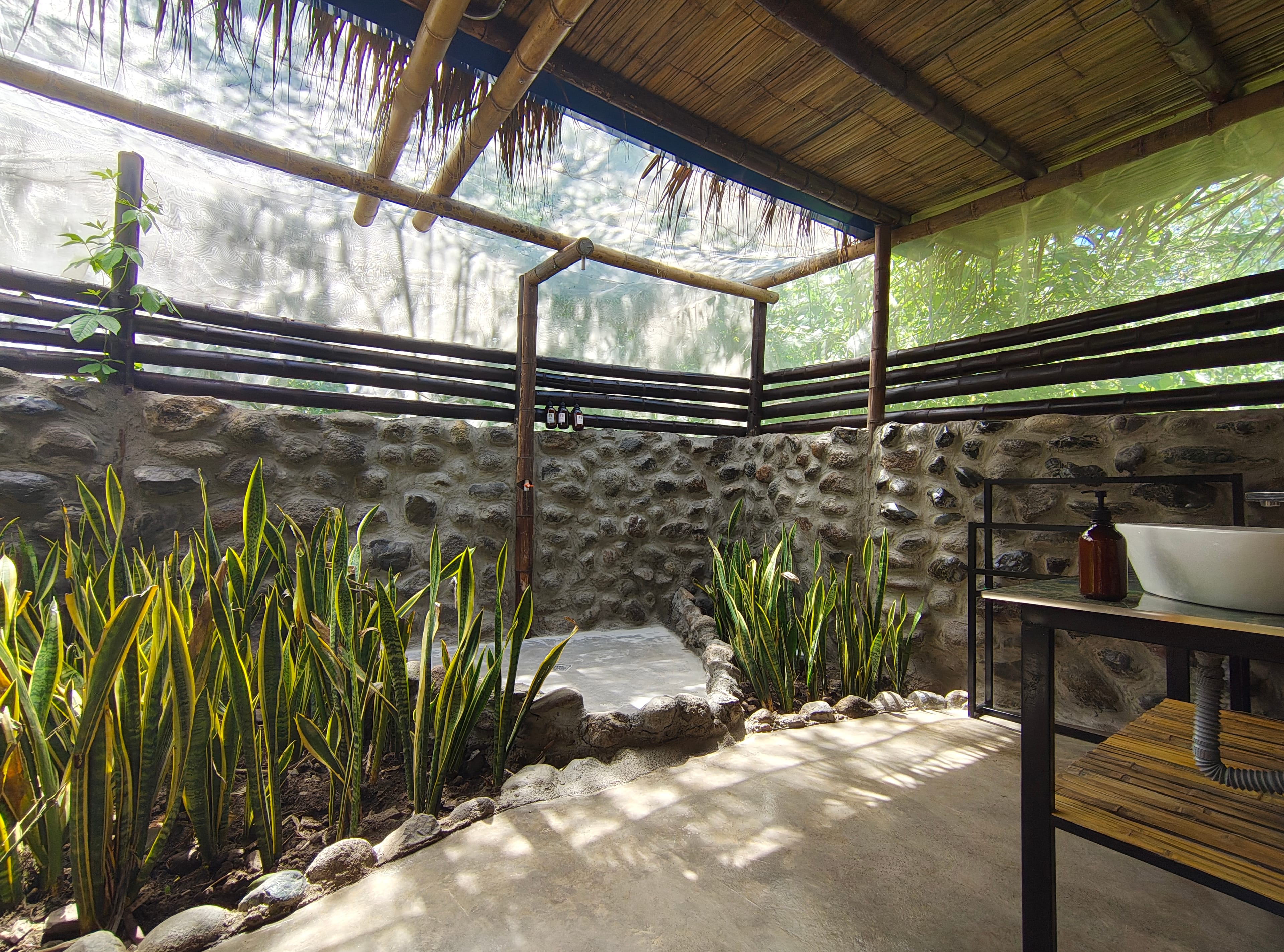 Baño completo al aire libre con ducha, plantas tropicales y luz natural