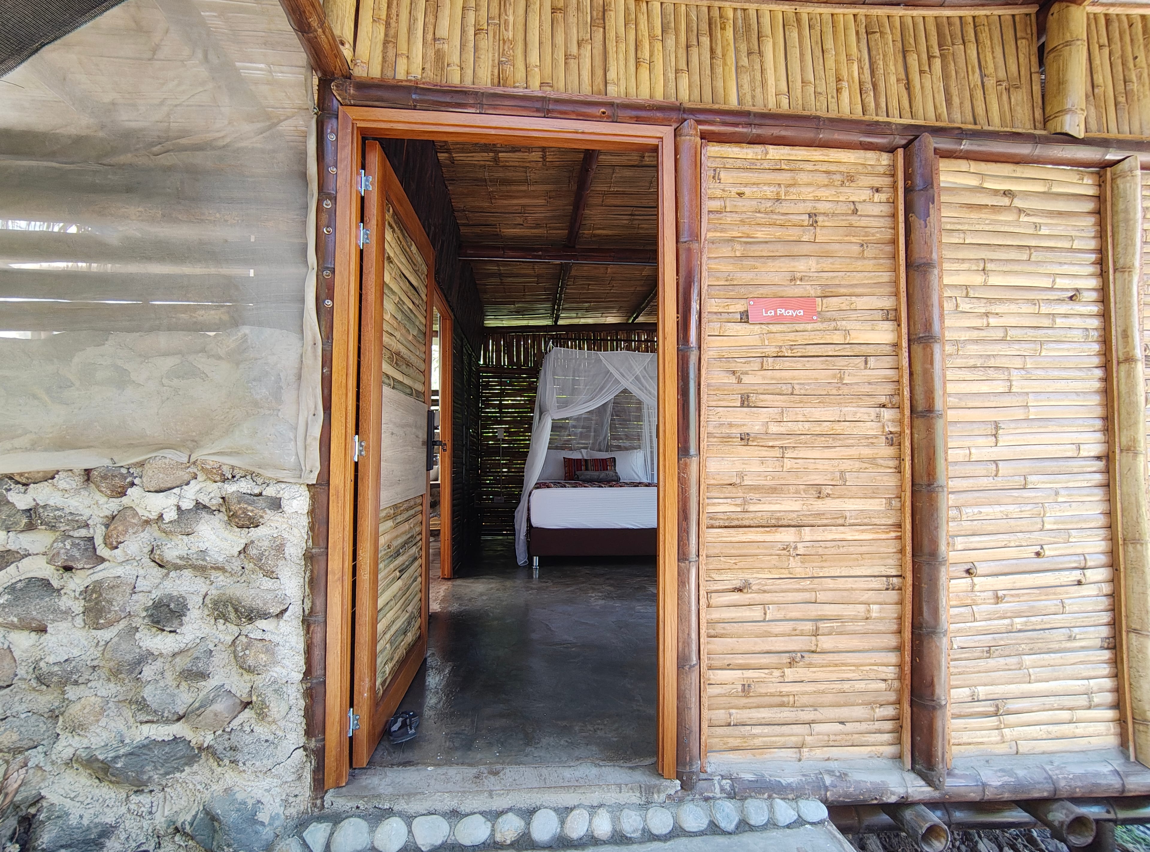Entrada al refugio con puertas de bambú y muro de piedra natural