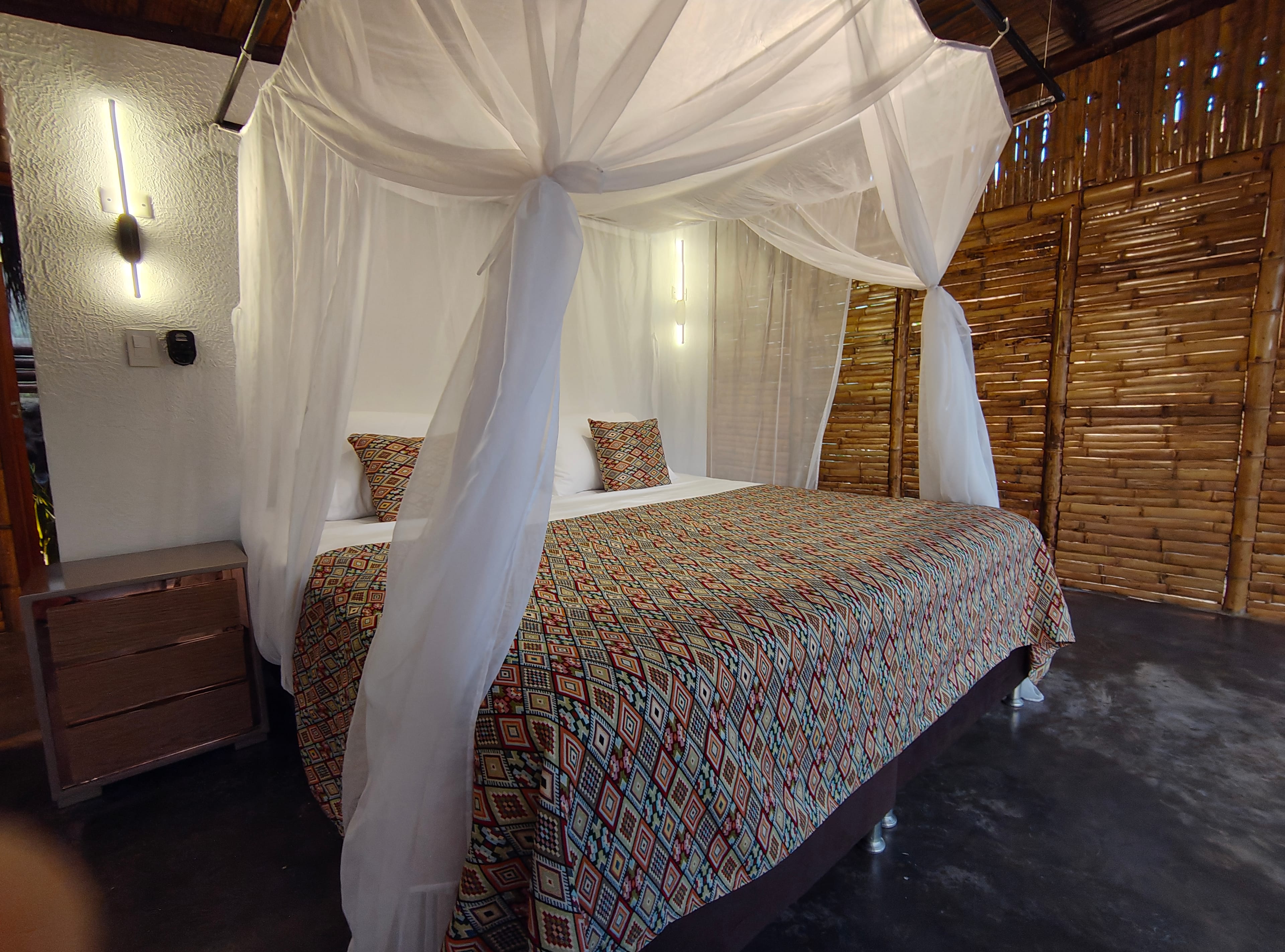 Cama king con mosquitero blanco, cobija artesanal de colores y paredes de bambú