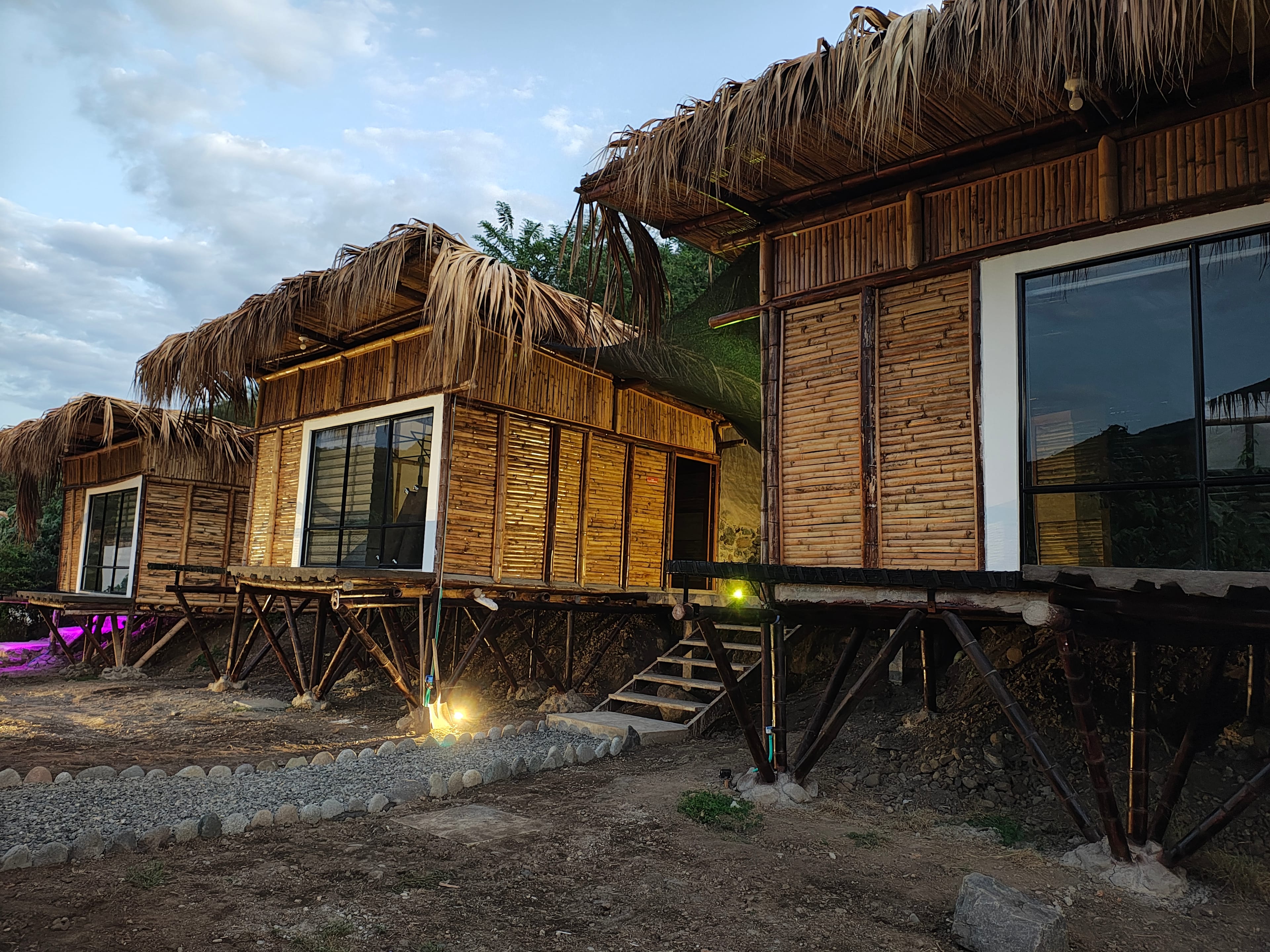 Vista exterior de Suite Raíz al atardecer con construcción de bambú y techo de paja