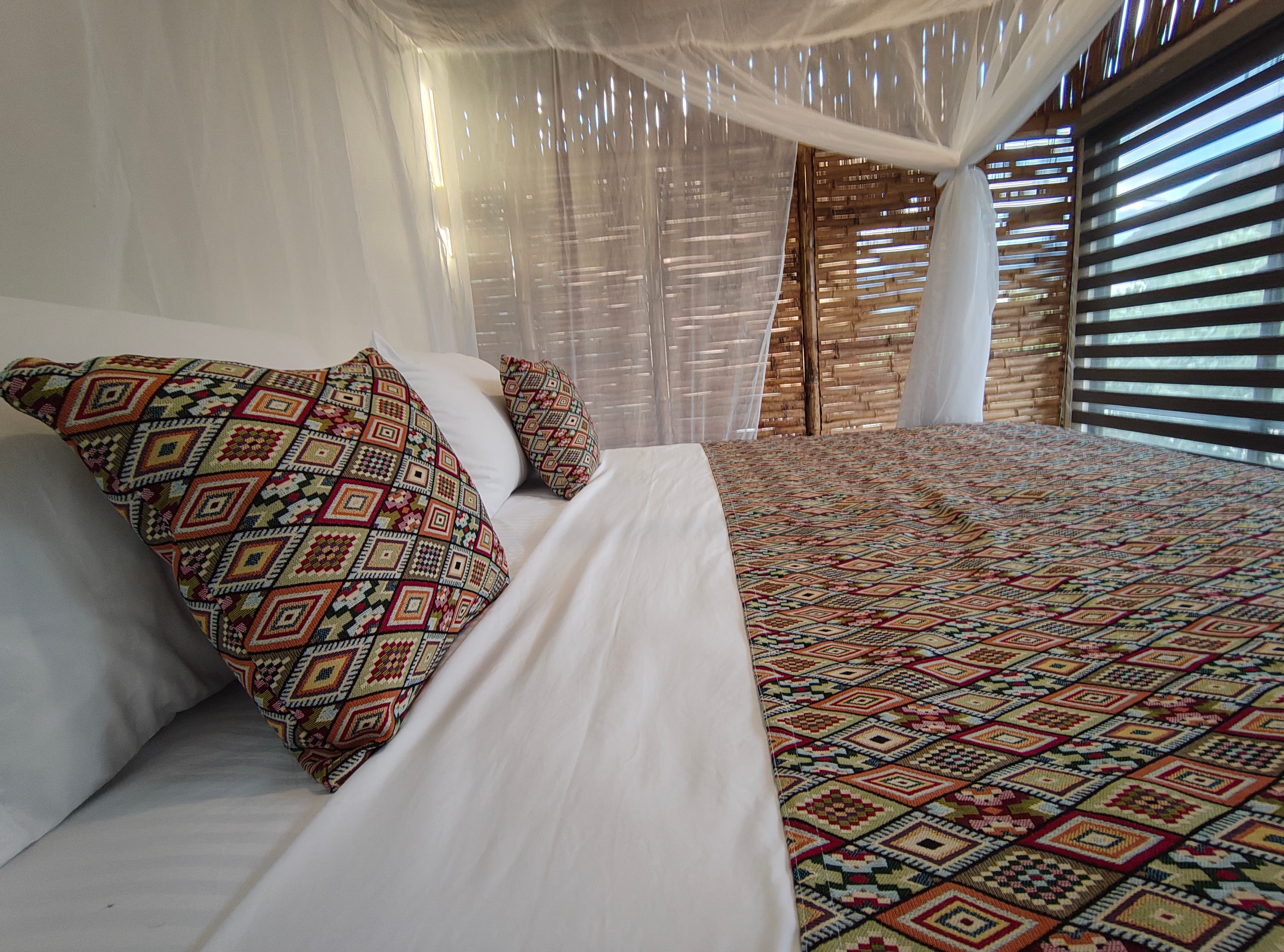 Cama king con textiles artesanales y ventanal con persiana de bambú sheer
