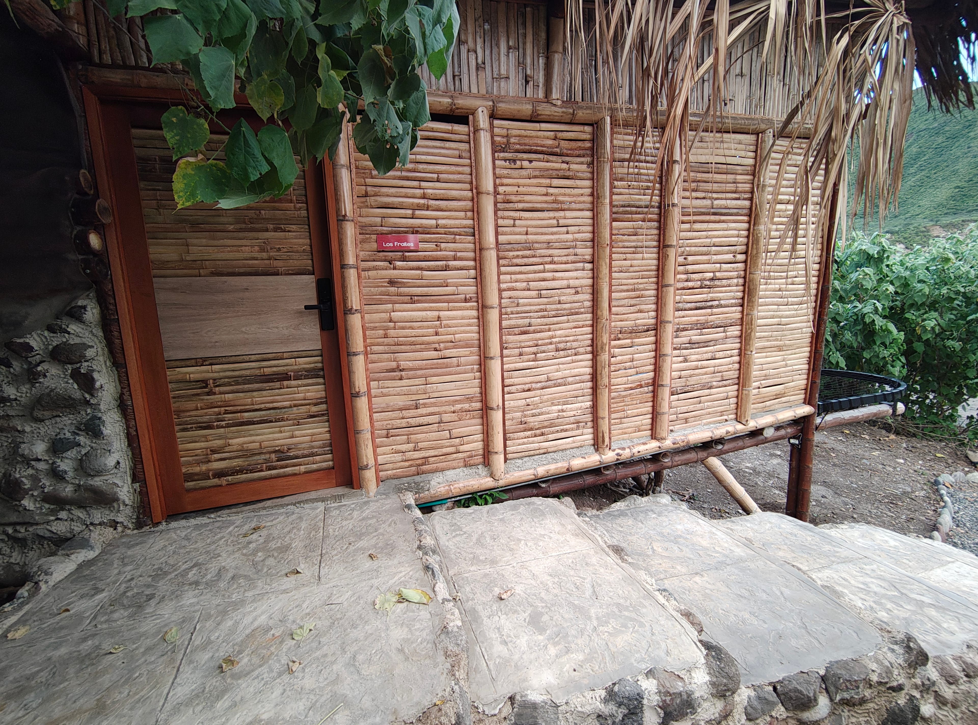 Entrada al refugio con puerta de bambú y vegetación tropical